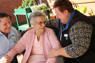 elderly aged care resident sitting down outside the nursing home with two baptistcare aged care workers